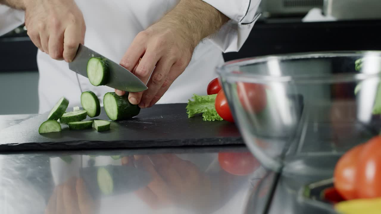hombre cortando pepino en el restaurante de la cocina. mano del chef preparando ensalada fresca