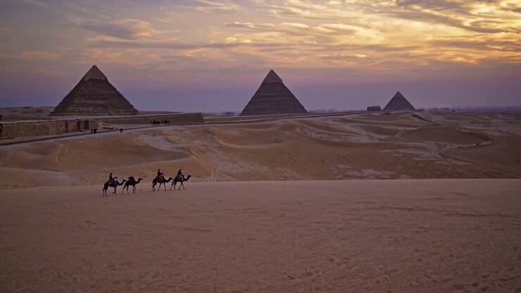 Video grandangolare di cammelli che attraversano il deserto al tramonto, con le piramidi