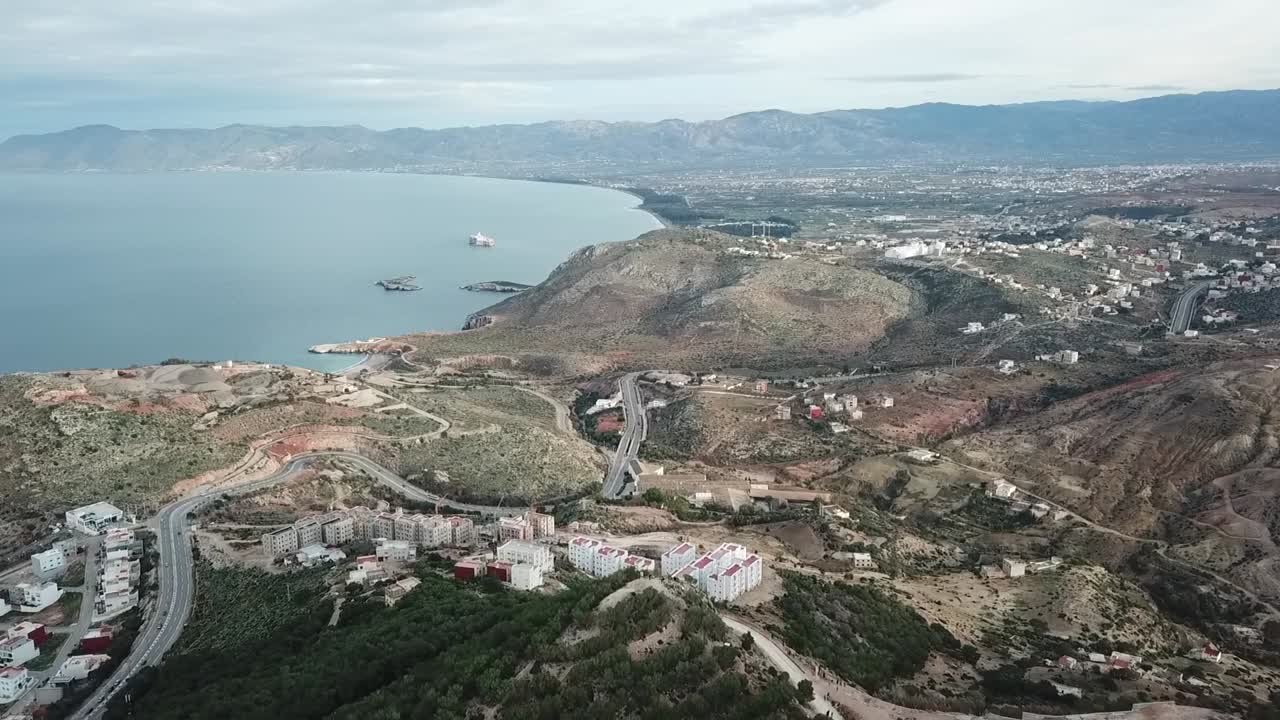 Drone footage showing white hillside homes in Al Hoceima. Scenic view of the Rif Mountains meeting the blue Mediterranean Sea coast in Morocco