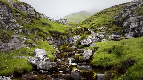 wild mountain river flowing down through stones in cold green mountain in the faroe islands