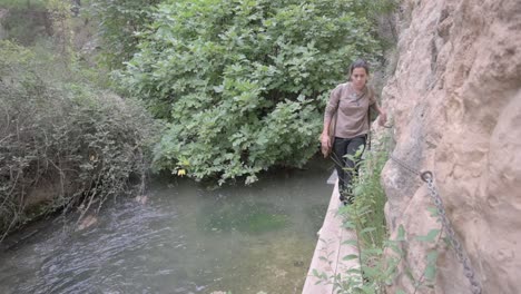 young brunette hiker walking carefully along wooden walkways over a river, surrounded by lush surroundings and flowing water