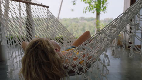 young woman in hammock swaying peacefully on lazy summer day enjoying vacation lifestyle at holiday resort