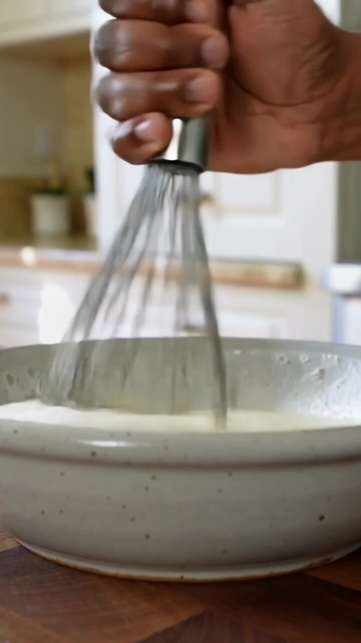 Video verticale: Una mano destra mescola un liquido con una frusta in una ciotola posta sul bancone della cucina