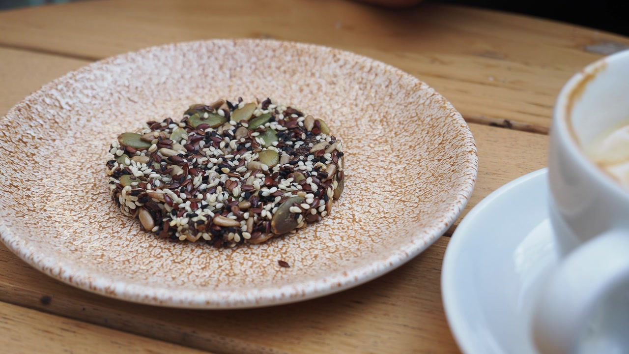 Hand Picking Up a Healthy Seed Cracker from a Plate Next to Coffee