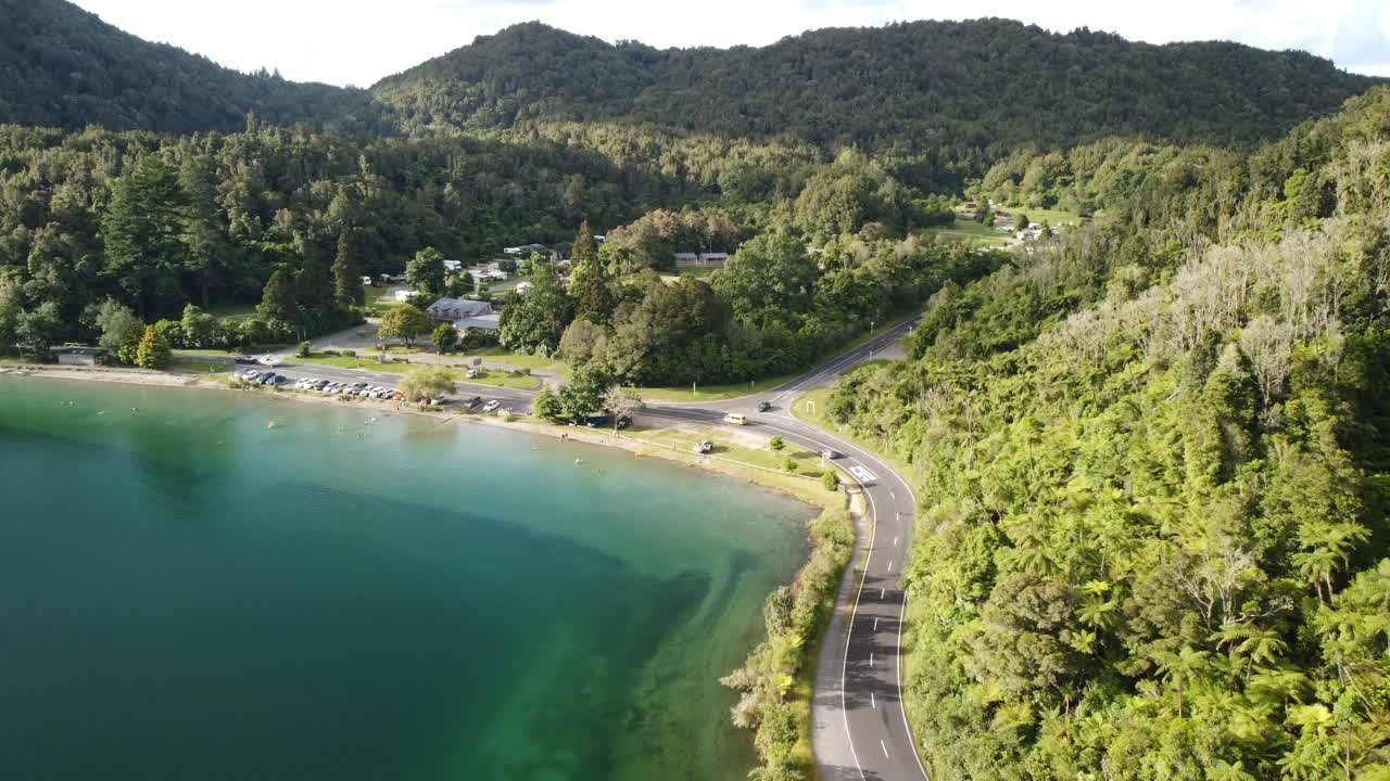 campamento de vacaciones junto al lago, lago azul, camino del bosque de palmeras y turista en paddle bord 4k drone disparado en nueva zelanda