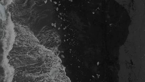 slow motion aerial shot directly above crashing waves on black sand beach