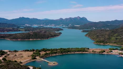 vuelo aéreo sobre el agua turquesa del embalse de la isla alta, verdes colinas y senderos durante el día, península de san kung en hong kong, china