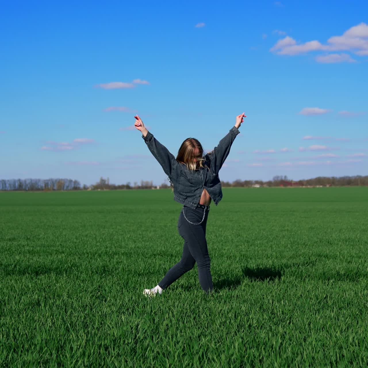 Happy young woman in spring day. Attractive girl in denim suit jumping happily on field in a bright day. Joyful girl on a green meadow