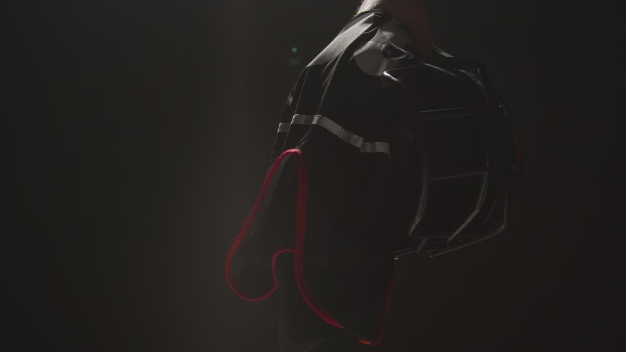 낮은 키 조명으로 헬멧과 팀 저지를 들고 있는 미국 축구 선수의 스튜디오 샷을 닫습니다.