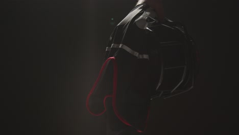 Close-Up-Studio-Shot-Of-American-Football-Player-Holding-Helmet-And-Team-Jersey-With-Low-Key-Lighting-