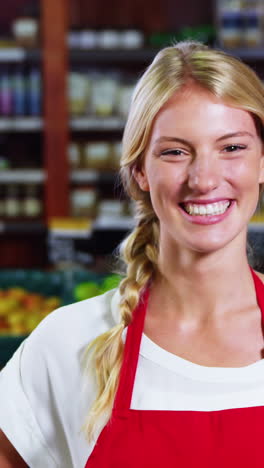 smiling female staff standing with hands on hip in grocery section