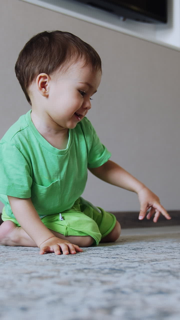 Smiling Caucasian boy sits on the floor playing with toy. Happy healthy child pushes his train. Vertical video