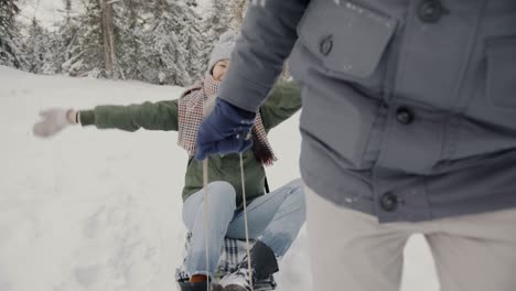 slow motion portrait of happy asian woman riding sled laughing talking to boyfriend in winter forest