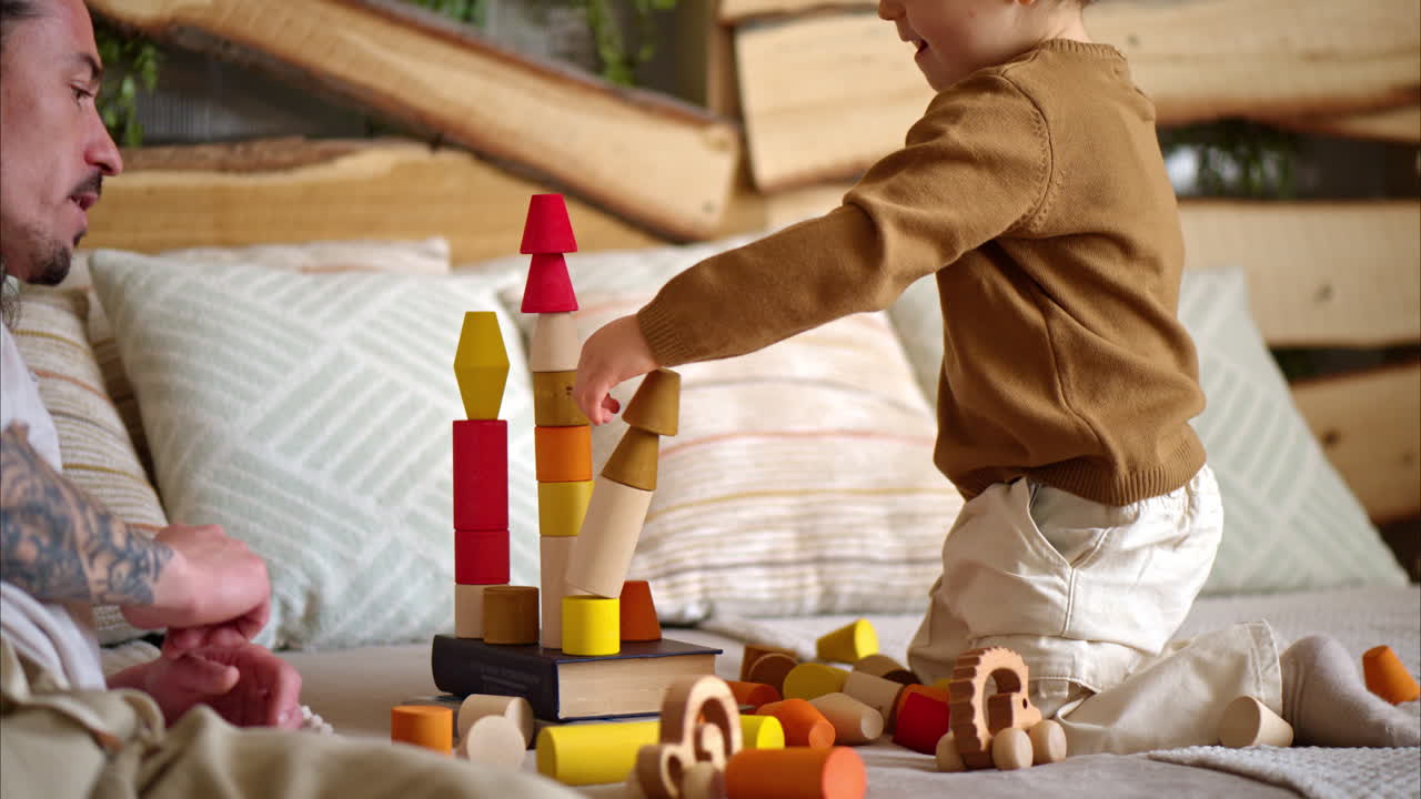 Father playing with his son with colourful, ecological wooden toys on the bed