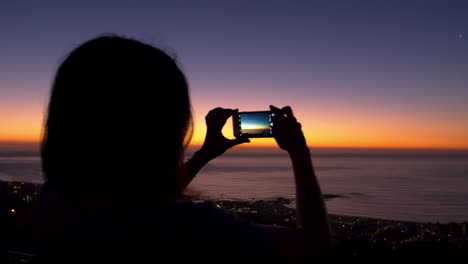 Woman-taking-photos-with-phone-on-beach,-silhouette-at-sunset