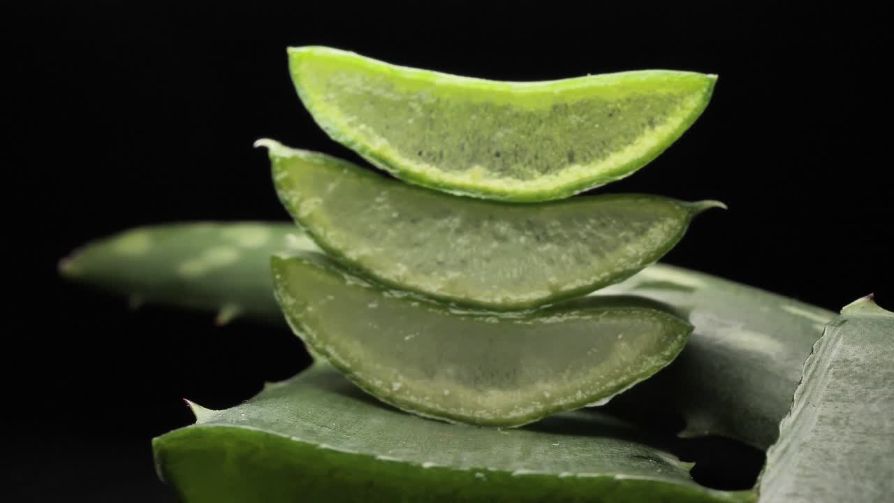 aloe vera fresco cortado en rodajas sobre fondo negro, concepto de hierba verde para la presentación de productos cosméticos y para el cuidado de la piel, movimiento suave y redondo