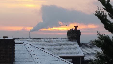 smoking energy industry chimney above frosty winter home rooftops glowing sunrise orange sky