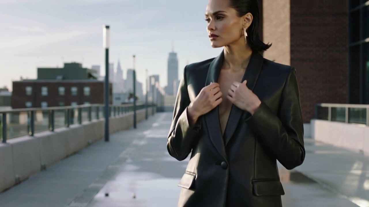 Modella che cammina entrando da sinistra, attraversando una terrazza sul tetto, sistemando un blazer scuro per un servizio fotografico di moda.