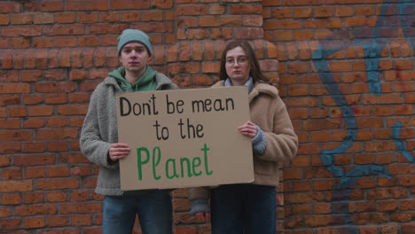 jóvenes activistas masculinos y femeninos mirando la cámara sosteniendo un cartel de cartón durante una protesta por el cambio climático