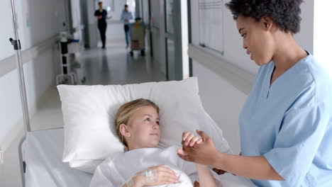 african american nurse cares for a caucasian girl in a hospital bed