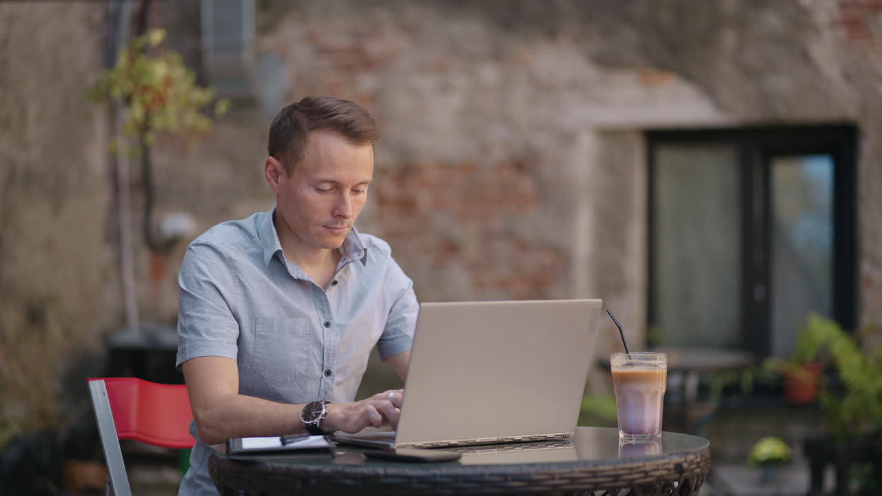 Freelancer businessman in glasses diligently working on laptop in cafe. Man typing on keyboard and searches new job on internet at coffee shop