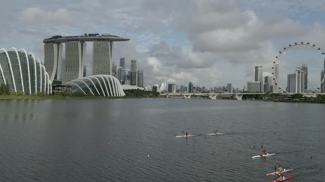Side flying drone shot tracking kayakers at Marina Bay with Gardens by the Bay - Marina Bay Sands in the backdrop (4K).mp4