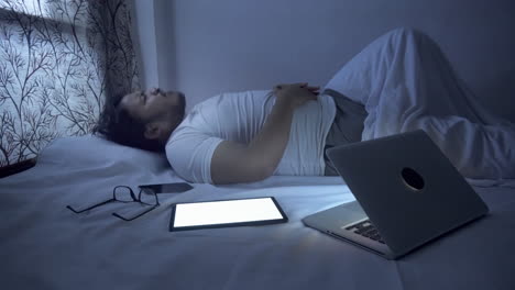 a man lying on the bed suffering from severe stomach pain, diarrhoea, he overworking with computer technology during night time