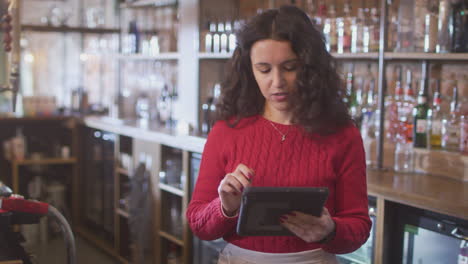 trabajadora de bar de pie detrás del mostrador comprobando el stock usando una tableta digital