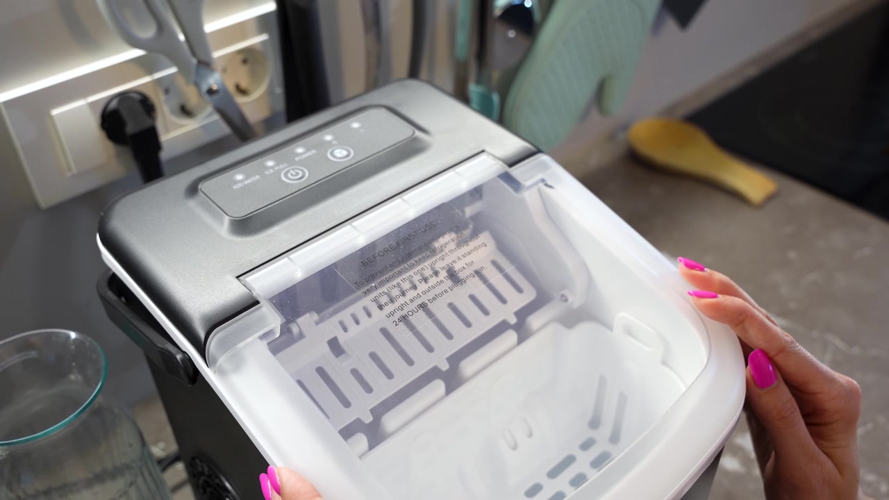 Woman Using Portable Countertop Ice Maker Appliance at Home Kitchen. Ideal for Concepts Related to Household Appliances, Domestic Lifestyle, Kitchen Technology, Domestic Living, Beverage Preparation.