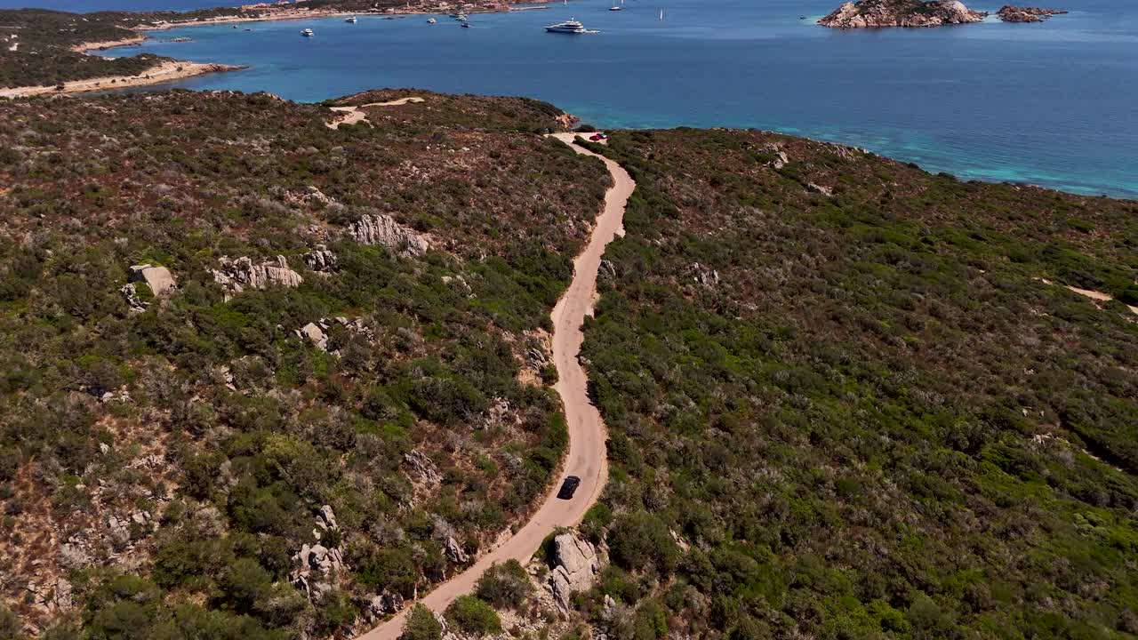 A car travels along Sardinian coastal road under sunny skies and blue waters