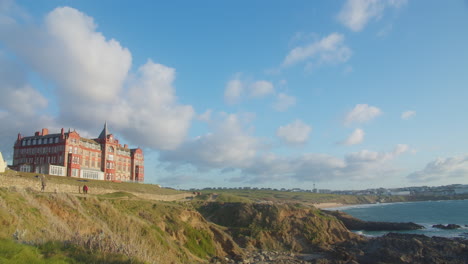 Hotel-De-Cabecera-En-La-Cima-De-Una-Colina-Con-Vistas-A-La-Playa-Fistral-Con-Turistas-Caminando-Por-El-Sendero-Que-Va-A-La-Playa-En-Cornualles,-Inglaterra---Lapso-De-Tiempo