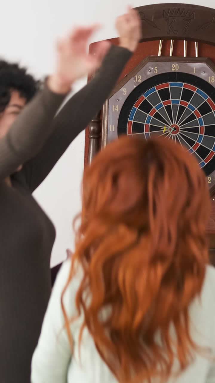 Cheerful woman playing game of dart with friends at home