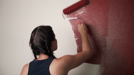 mujer joven pinta pared roja en casa