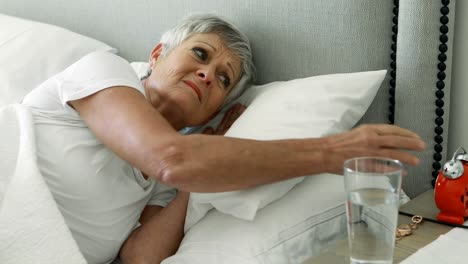 mujer mayor apagando el reloj despertador en el dormitorio