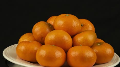 Plate-of-Clementine-oranges-revolves-on-small-white-platter-on-black