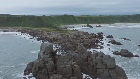 Aerial-view-Tasman-Sea-and-white-wash-waves-breaking-against-rocky-headland-shoreline-at-Cape-Foulwind-on-West-Coast,-South-Island-of-New-Zealand-Aotearoa