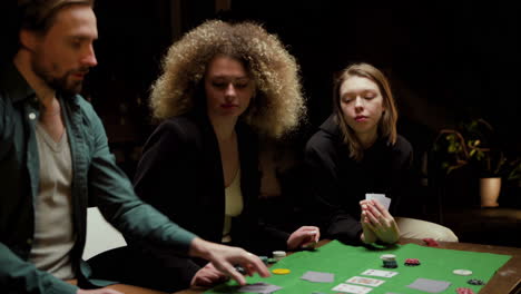 Group-Of-Friends-Playing-Poker-Sitting-On-Chairs-At-A-Table-At-Home