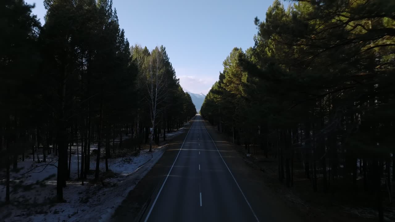 Riprese drone di una lunga e dritta strada asfaltata che attraversa una fitta pineta con montagne distanti all'orizzonte, vicino al villaggio di Arshan, Buriazia, Russia.