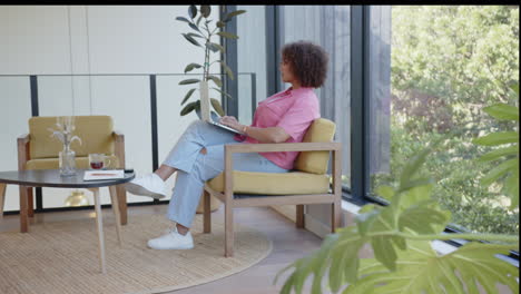 sitting in chair, woman holding tablet and relaxing in modern living room