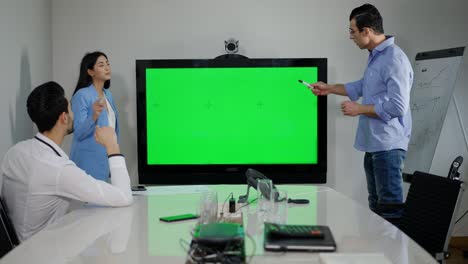 confiados colegas multiétnicos del milenio discutiendo proyectos en la oficina con monitor de pantalla verde. mujer asiática concentrada y hombres de oriente medio haciendo lluvia de ideas en el interior con pantalla chromakey.