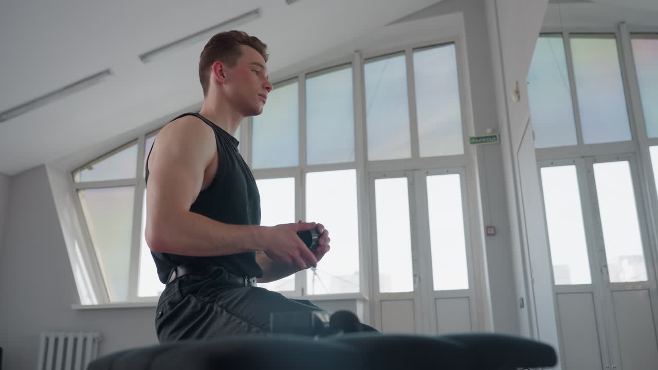 student seated before mirror opens hair cream container retrieves smooth styling cream closes container returns it to seat then rubs cream into hands in bright loft studio setting