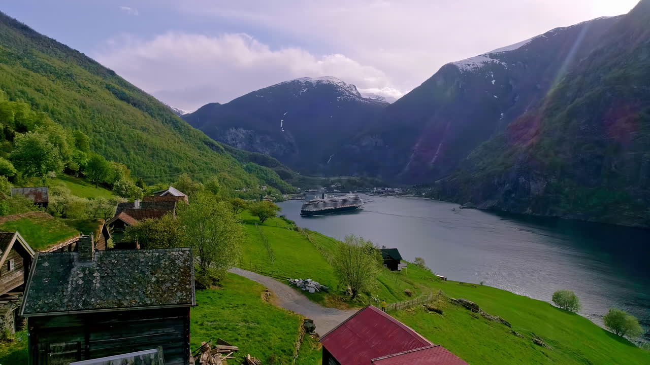 valle verde con casas y un lago con un crucero entre altas montañas y un cielo con nubes