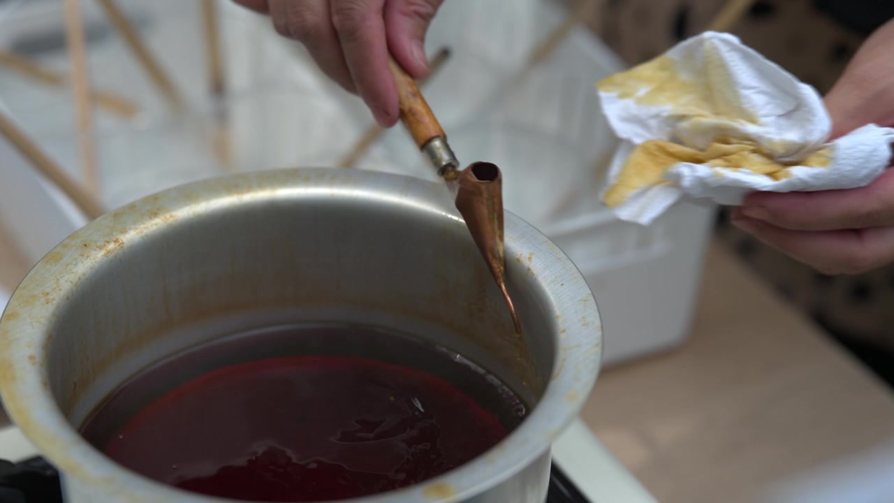 Primo piano di un artigiano che immerge un canting in un contenitore di cera fusa per la tecnica batik