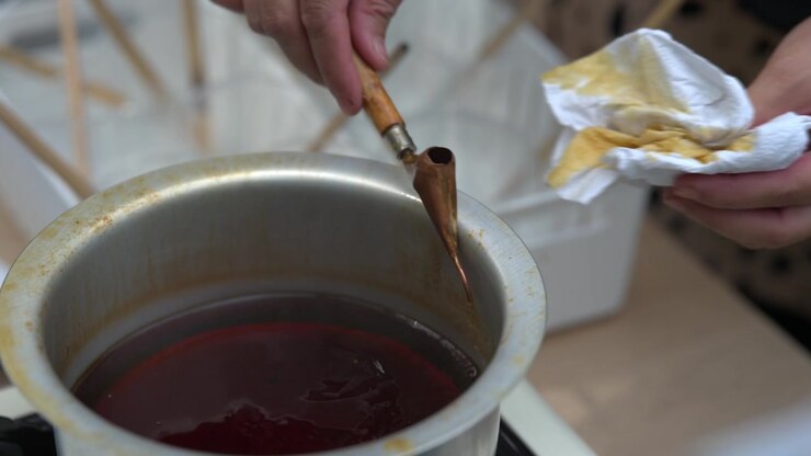 Primo piano di un artigiano che immerge un canting in un contenitore di cera fusa per la tecnica batik