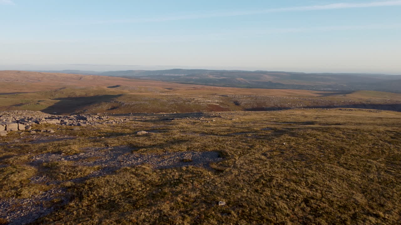 un dron aéreo de 4k panorámico y moviéndose en un paisaje rocoso con un parque eólico y campos en segundo plano en brecon beacons, gales, reino unido