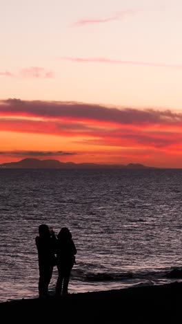 couple taking photos of sunset over the ocean