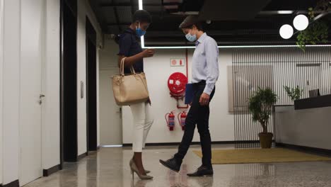 diverse business people wearing face masks greeting in corridor using feet