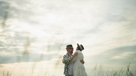 a joyful couple embraces in a grassy field, both wearing hats. the woman is dressed in a white dress, and the man in a checkered shirt. the scene captures their happiness and love in a serene