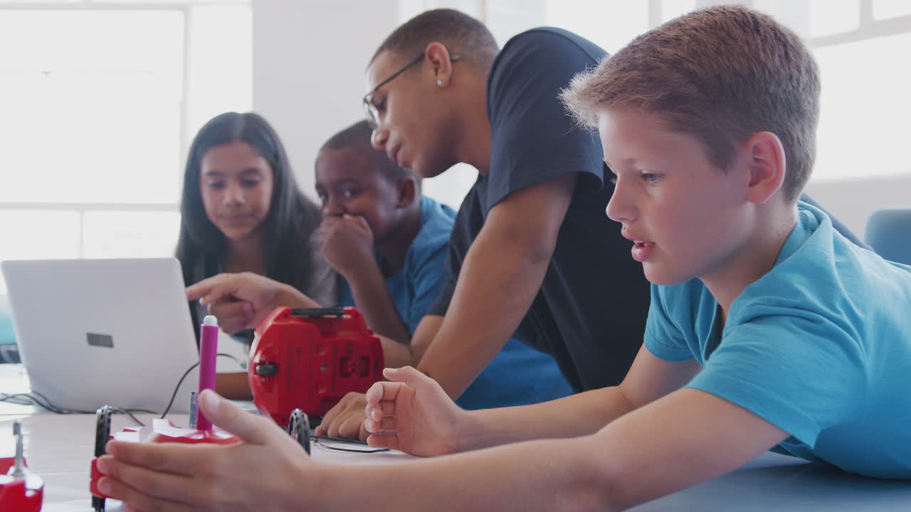 Students With Male Teacher In After School Computer Coding Class Learning To Program Robot Vehicle
