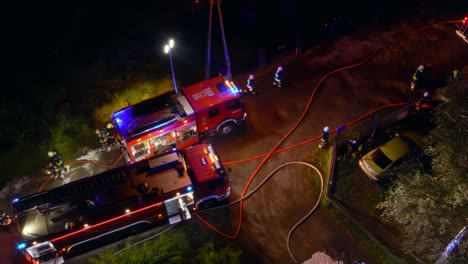 a tangle of fire engines and fire hoses seen from above on a dirt road at night